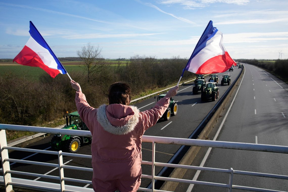 En kvinde på en motorvejsbro lige syd for Pairs hilser demonstrerende landmænd på traktorer, mens de vifter med franske flag den 26. januar 2024. Foto: Christophe Ena / AP / NTB. En kvinde på en motorvejsbro lige syd for Pairs hilser demonstrerende landmænd på traktorer, mens de vifter med franske flag den 26. januar 2024. Foto: Christophe Ena / AP / NTB.