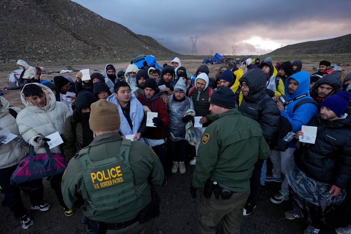 U.S. Border Patrol agents, front, speak with migrants seeking asylum, mainly from Colombia, China and Ecuador, in a makeshift, mountainous campsite after crossing the border between Mexico and the United States, Friday, Feb. 2, 2024, near Jacumba, Calif. About 200 migrants huddled under blankets and plastic bags under pounding rain and wind Friday night, as Border Patrol agents tried to work out transportation to area facilities. (AP Photo/Gregory Bull) U.S. Border Patrol agents, front, speak with migrants seeking asylum, mainly from Colombia, China and Ecuador, in a makeshift, mountainous campsite after crossing the border between Mexico and the United States, Friday, Feb. 2, 2024, near Jacumba, Calif. About 200 migrants huddled under blankets and plastic bags under pounding rain and wind Friday night, as Border Patrol agents tried to work out transportation to area facilities. (AP Photo/Gregory Bull)