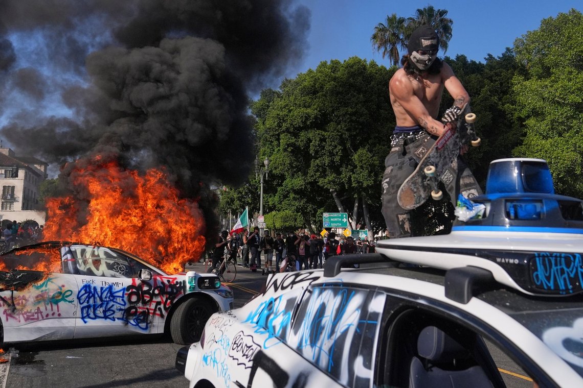 A protester vandalizes a Waymo taxi as another burns near the metropolitan detention center of downtown Los Angeles, Sunday, June 8, 2025, following last night's immigration raid protest. (AP Photo/Jae C. Hong) A protester vandalizes a Waymo taxi as another burns near the metropolitan detention center of downtown Los Angeles, Sunday, June 8, 2025, following last night's immigration raid protest. (AP Photo/Jae C. Hong)