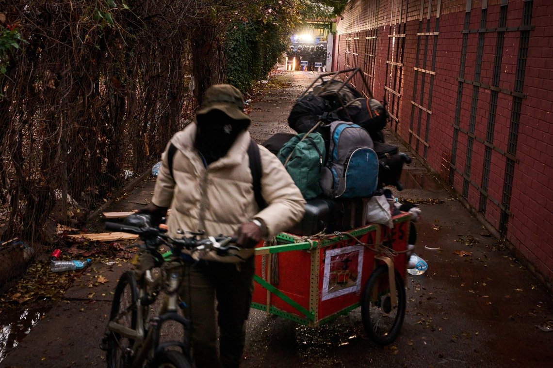 A migrant carries his belongings as police, in the background, prepares to carry out eviction orders at an abandoned school building where hundreds of mostly undocumented migrants had been living, in Badalona, near Barcelona, Spain, Wednesday, Dec. 17, 2025. (AP Photo/Emilio Morenatti) A migrant carries his belongings as police, in the background, prepares to carry out eviction orders at an abandoned school building where hundreds of mostly undocumented migrants had been living, in Badalona, near Barcelona, Spain, Wednesday, Dec. 17, 2025. (AP Photo/Emilio Morenatti)