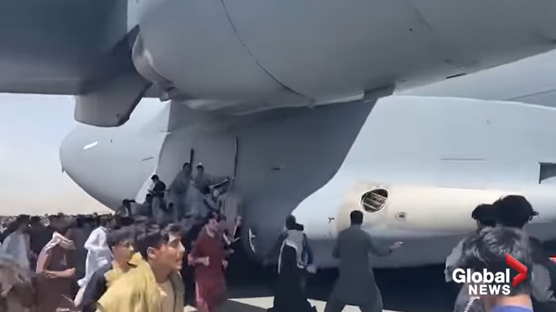 Desperate Afghans tried to get to the US by hanging from the outside of a military transport plane. Biden blames Trump for the chaos. Screenshot YouTube/ Global News Desperate Afghans tried to get to the US by hanging from the outside of a military transport plane. Biden blames Trump for the chaos. Screenshot YouTube/ Global News