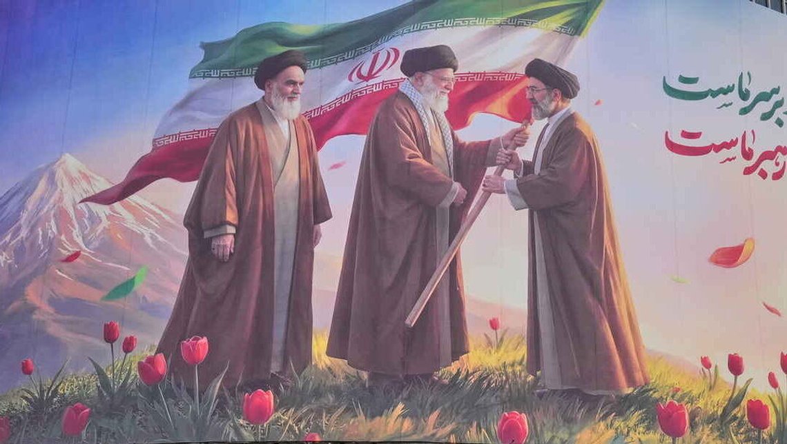 A poster showing Iran’s recently killed leader, Ali Khamenei, handing the Iranian flag to his son Mojtaba Khamenei, while Iran’s former leader Ruhollah Khomeini looks on as the mantle of leadership is passed. A poster showing Iran’s recently killed leader, Ali Khamenei, handing the Iranian flag to his son Mojtaba Khamenei, while Iran’s former leader Ruhollah Khomeini looks on as the mantle of leadership is passed.