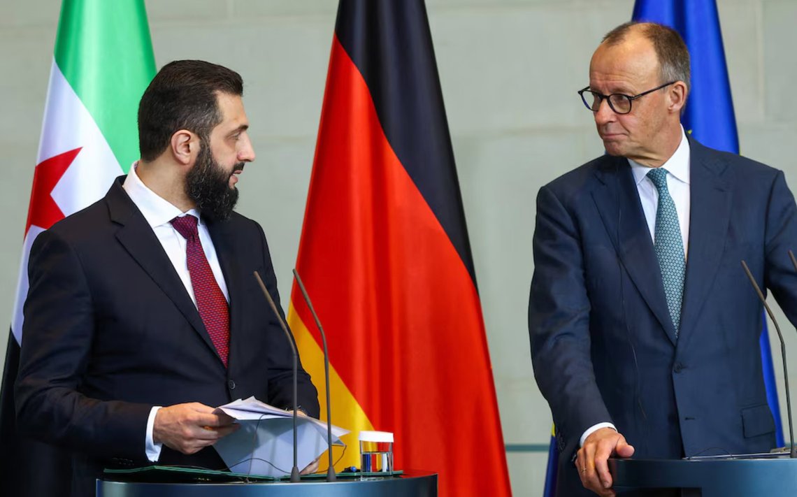 Syrian President Ahmed Sharaa speaks during a joint press conference with German Chancellor Friedrich Merz in Berlin, while Merz listens attentively. March 2026. Video still. Syrian President Ahmed Sharaa speaks during a joint press conference with German Chancellor Friedrich Merz in Berlin, while Merz listens attentively. March 2026. Video still.