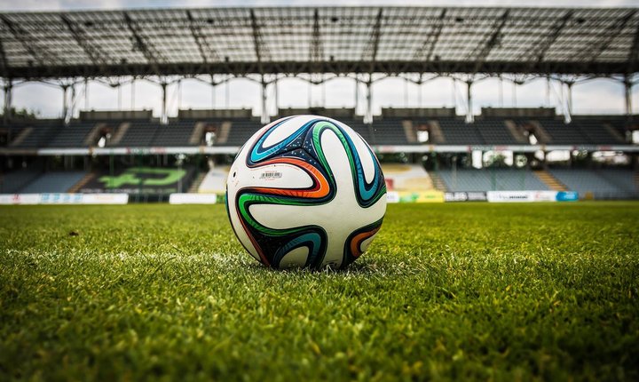 Soccer ball resting on green grass inside an empty football stadium.