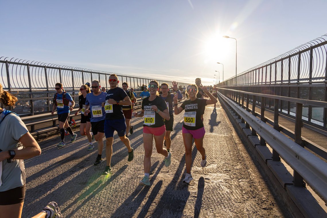 Participants in the Midnight Sun Marathon run across a bridge in Tromsø under the low Arctic sun. Photo: Zoltan Tot. Runners take part in the Midnight Sun Marathon in Tromsø, crossing a bridge in bright evening sunlight.