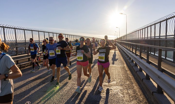 Runners take part in the Midnight Sun Marathon in Tromsø, crossing a bridge in bright evening sunlight.
