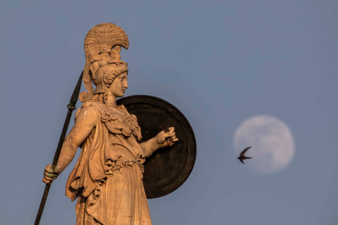 The flower moon rises behind the statue of the ancient Greek goddess of wisdom, Athena, atop the Academy of Athens building as a pigeon flies, on Monday, May 24, 2021. The flower moon rises behind the statue of the ancient Greek goddess of wisdom, Athena, atop the Academy of Athens building as a pigeon flies, on Monday, May 24, 2021.