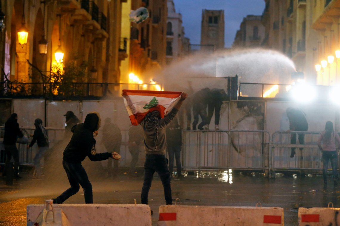 A demonstrator holds up a national flag as police use water cannon during a protest against the newly formed government in Beirut, Lebanon January 22, 2020. REUTERS/Mohamed Azakir A demonstrator holds up a national flag as police use water cannon during a protest against the newly formed government in Beirut, Lebanon January 22, 2020. REUTERS/Mohamed Azakir