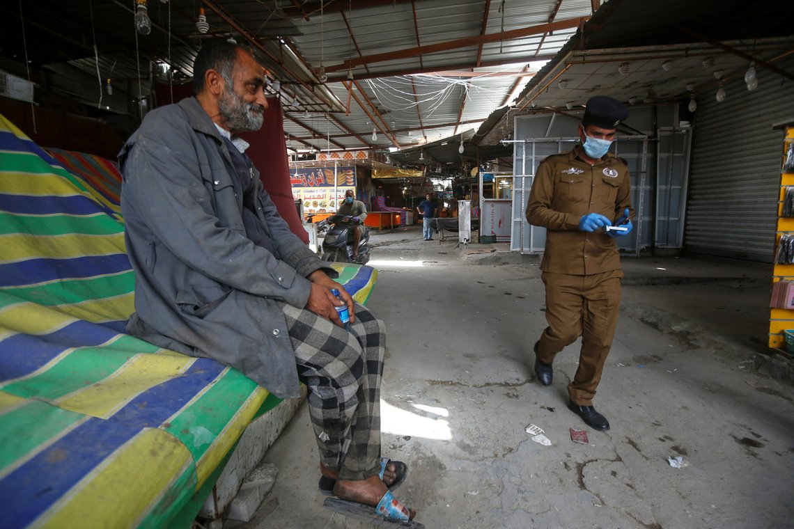 An Iraqi police officer wearing a protective face mask and gloves walks near a homeless man, who sits at a closed popular market in Basra, during a curfew imposed to prevent the spread of coronavirus disease (COVID-19), in Basra, Iraq April 2, 2020. REUTERS/Essam al-Sudani An Iraqi police officer wearing a protective face mask and gloves walks near a homeless man, who sits at a closed popular market in Basra, during a curfew imposed to prevent the spread of coronavirus disease (COVID-19), in Basra, Iraq April 2, 2020. REUTERS/Essam al-Sudani