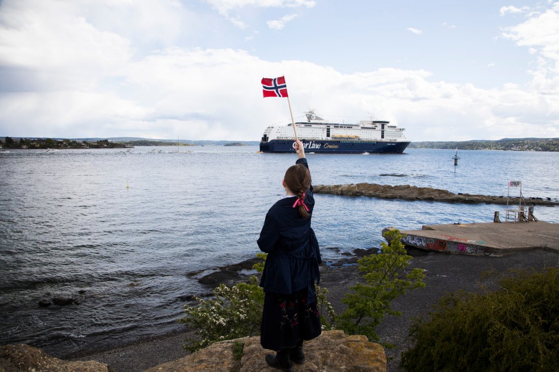 Oslo 20200517.
En jente står på Hukodden på Bygdøy i Oslo og med vifter sitt flagg mot fergen Color Magic. Cruisefergen seiler vanligvis i fast rute mellom Oslo og Kiel, men som en følge av korona-pandemien og vedtakene fra regjeringen om å stenge grensene og unngå fritidsreiser, har Color Magic og søsterskipet Color Fantasy ligget i opplag i Oslo siden 14. mars. På nasjonaldagen pyntet rederiet skipet og inviterte til en seilas og båtkonvoi på fjorden.
Foto: Erik Johansen / NTB scanpix Oslo 20200517.
En jente står på Hukodden på Bygdøy i Oslo og med vifter sitt flagg mot fergen Color Magic. Cruisefergen seiler vanligvis i fast rute mellom Oslo og Kiel, men som en følge av korona-pandemien og vedtakene fra regjeringen om å stenge grensene og unngå fritidsreiser, har Color Magic og søsterskipet Color Fantasy ligget i opplag i Oslo siden 14. mars. På nasjonaldagen pyntet rederiet skipet og inviterte til en seilas og båtkonvoi på fjorden.
Foto: Erik Johansen / NTB scanpix