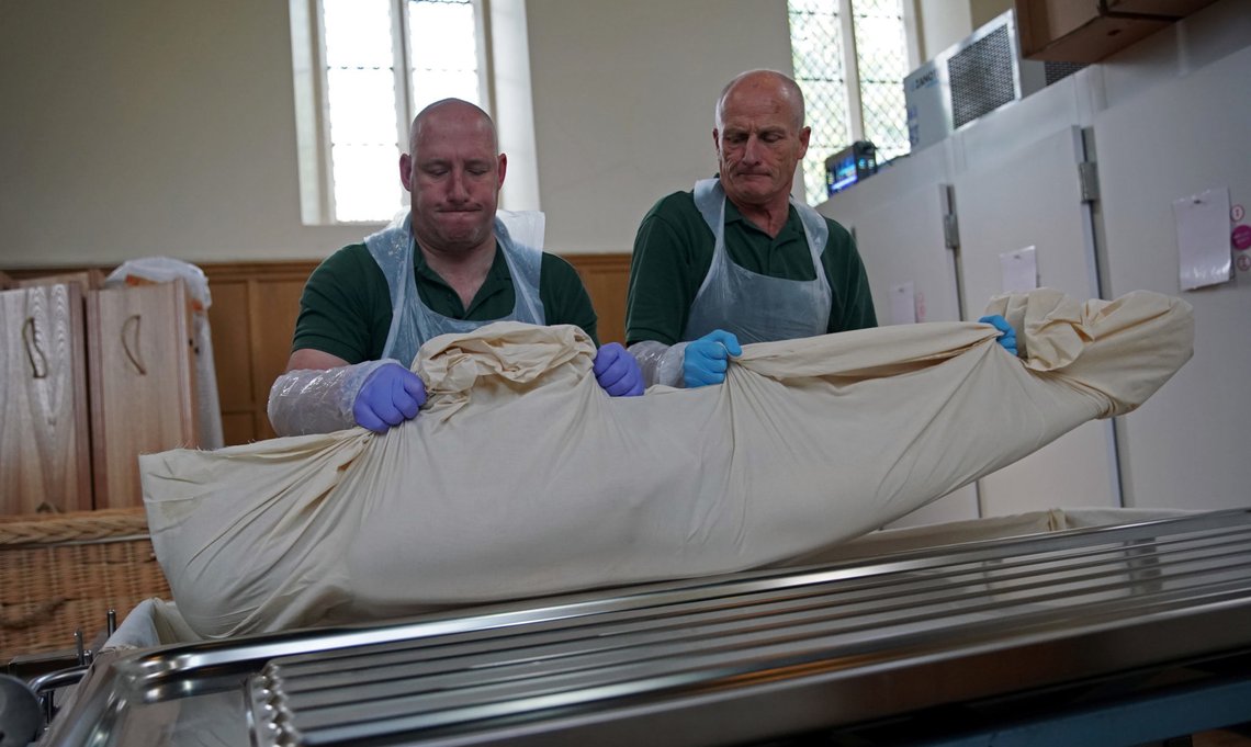 Mortuary workers Stuart Emans and Graham Cowper move the body of a deceased person from a trolley to a coffin in the mortuary at Poppy's Funerals in Lambeth Cemetery, as the spread of the coronavirus disease (COVID-19) continues in London, Britain, May 4, 2020. Picture taken May 4. REUTERS/Hannah McKay Mortuary workers Stuart Emans and Graham Cowper move the body of a deceased person from a trolley to a coffin in the mortuary at Poppy's Funerals in Lambeth Cemetery, as the spread of the coronavirus disease (COVID-19) continues in London, Britain, May 4, 2020. Picture taken May 4. REUTERS/Hannah McKay