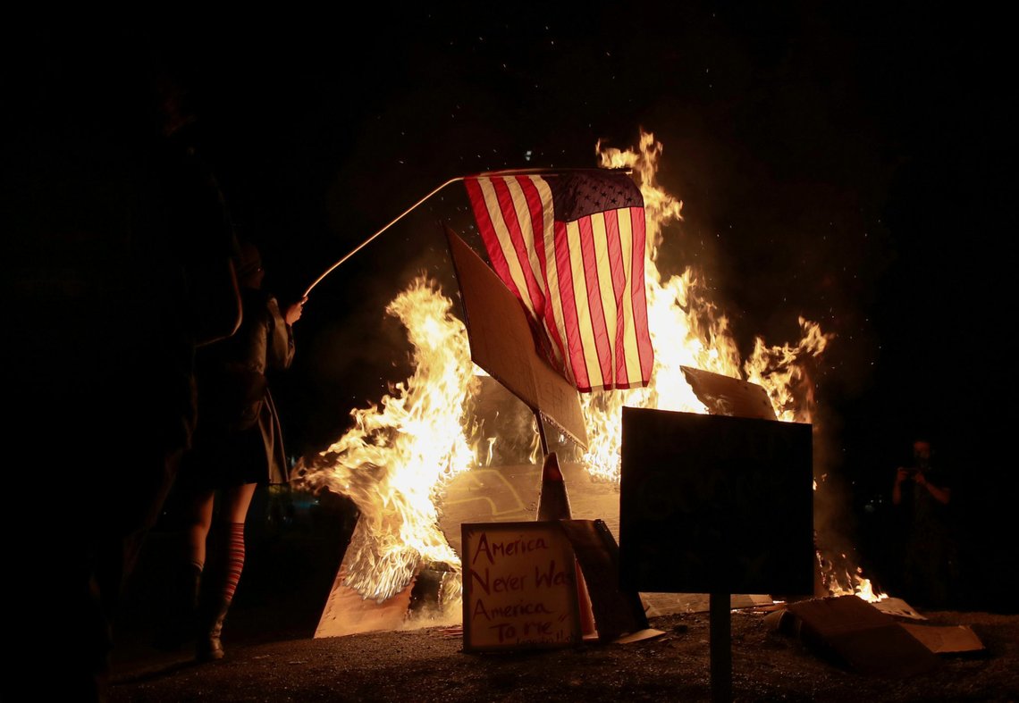 A demonstrator sets fire to an American flag during a protest against racial inequality and police violence in Portland, Oregon, U.S., July 27, 2020. REUTERS/Caitlin Ochs A demonstrator sets fire to an American flag during a protest against racial inequality and police violence in Portland, Oregon, U.S., July 27, 2020. REUTERS/Caitlin Ochs
