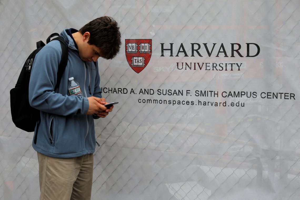 FILE PHOTO: A man looks at his mobile phone beside a sign for Harvard University in Cambridge, Massachusetts, U.S., June 18, 2018. REUTERS/Brian Snyder/File Photo FILE PHOTO: A man looks at his mobile phone beside a sign for Harvard University in Cambridge, Massachusetts, U.S., June 18, 2018. REUTERS/Brian Snyder/File Photo