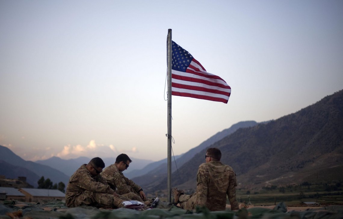 FILE - In this Sept. 11, 2011 file photo, US soldiers sit beneath an American flag just raised to commemorate the tenth anniversary of the 9/11 attacks at Forward Operating Base Bostick in Kunar province, Afghanistan. The Biden administrations surprise announcement in April 2021, of an unconditional troop withdrawal from Afghanistan by Sept. 11, 2021, appears to strip the Taliban and the Afghan government of considerable leverage, pressuring them to reach a peace deal. (AP Photo/David Goldman, File) FILE - In this Sept. 11, 2011 file photo, US soldiers sit beneath an American flag just raised to commemorate the tenth anniversary of the 9/11 attacks at Forward Operating Base Bostick in Kunar province, Afghanistan. The Biden administrations surprise announcement in April 2021, of an unconditional troop withdrawal from Afghanistan by Sept. 11, 2021, appears to strip the Taliban and the Afghan government of considerable leverage, pressuring them to reach a peace deal. (AP Photo/David Goldman, File)