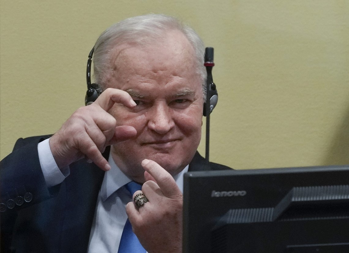 Former Bosnian Serb military chief Ratko Mladic imitates taking pictures as he sits the court room in The Hague, Netherlands, Tuesday, June 8, 2021, where the United Nations court delivers its verdict in the appeal of Mladic against his convictions for genocide and other crimes and his life sentence for masterminding atrocities throughout the Bosnian war. (AP Photo/Peter Dejong, Pool) Former Bosnian Serb military chief Ratko Mladic imitates taking pictures as he sits the court room in The Hague, Netherlands, Tuesday, June 8, 2021, where the United Nations court delivers its verdict in the appeal of Mladic against his convictions for genocide and other crimes and his life sentence for masterminding atrocities throughout the Bosnian war. (AP Photo/Peter Dejong, Pool)