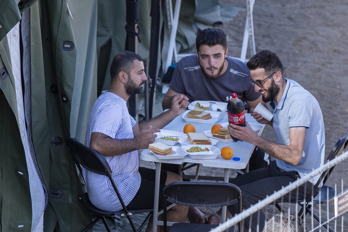 Migranter sitter utenfor et telt mens de spiser middag i den nybygde flyktningeleiren i byen Pabrade, rundt 40 km nordøst for Vilnius, Litauen, lørdag 3. juli 2021. EU-medlem Litauen har erklært unntakstilstand på grunn av tilstrømningen av migranter fra nabolandet Hviterussland de siste dagene. Litauens innenriksminister sa fredag at avgjørelsen, som ble foreslått av State Border Guard Service, ikke var nødvendig på grunn av økte trusler mot landet på 2,8 millioner, men å få på plass et mer robust system for å håndtere migranter. Foto: Mindaugas Kulbis / AP /NTB Migranter sitter utenfor et telt mens de spiser middag i den nybygde flyktningeleiren i byen Pabrade, rundt 40 km nordøst for Vilnius, Litauen, lørdag 3. juli 2021. EU-medlem Litauen har erklært unntakstilstand på grunn av tilstrømningen av migranter fra nabolandet Hviterussland de siste dagene. Litauens innenriksminister sa fredag at avgjørelsen, som ble foreslått av State Border Guard Service, ikke var nødvendig på grunn av økte trusler mot landet på 2,8 millioner, men å få på plass et mer robust system for å håndtere migranter. Foto: Mindaugas Kulbis / AP /NTB