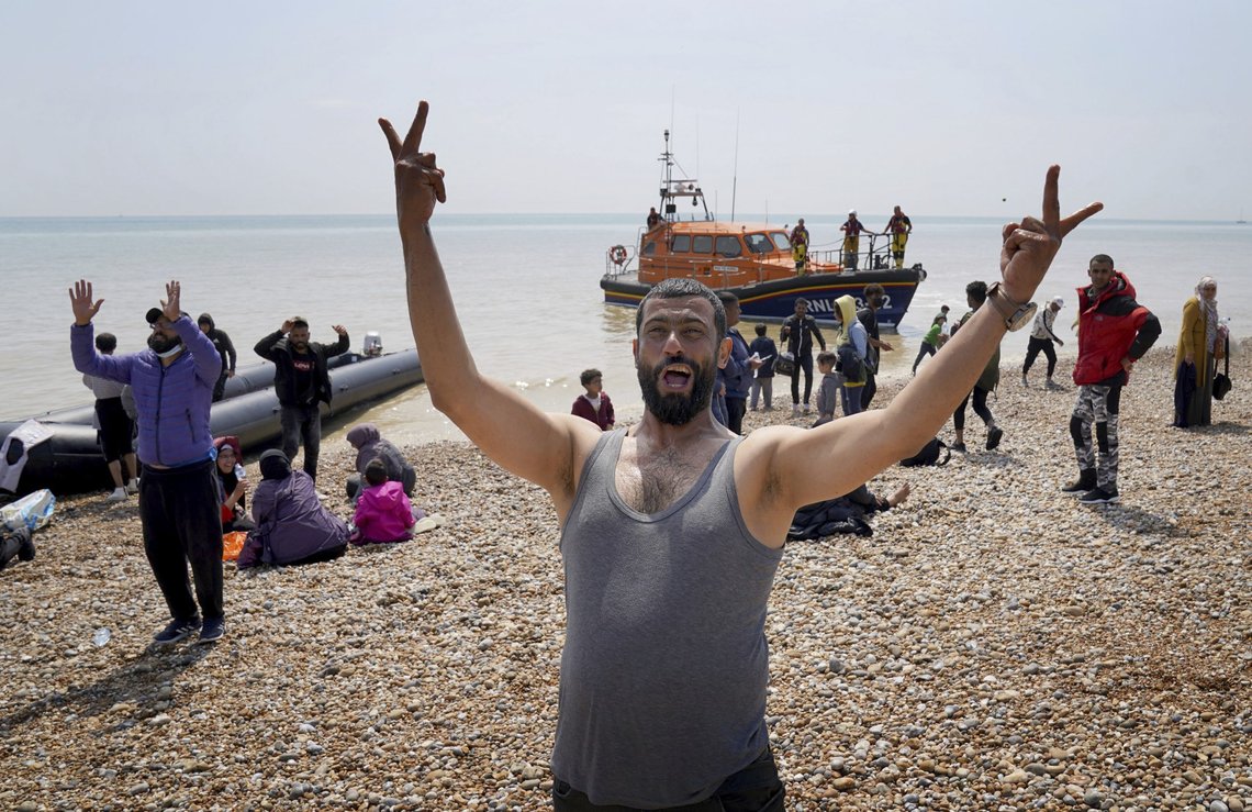 A man gestures as people thought to be migrants stand on the beach after arriving on a small boat at Dungeness in Kent, England, Monday July 19, 2021. They were later taken away by Border Force staff. (Gareth Fuller/PA via AP)(/PA via AP) A man gestures as people thought to be migrants stand on the beach after arriving on a small boat at Dungeness in Kent, England, Monday July 19, 2021. They were later taken away by Border Force staff. (Gareth Fuller/PA via AP)(/PA via AP)