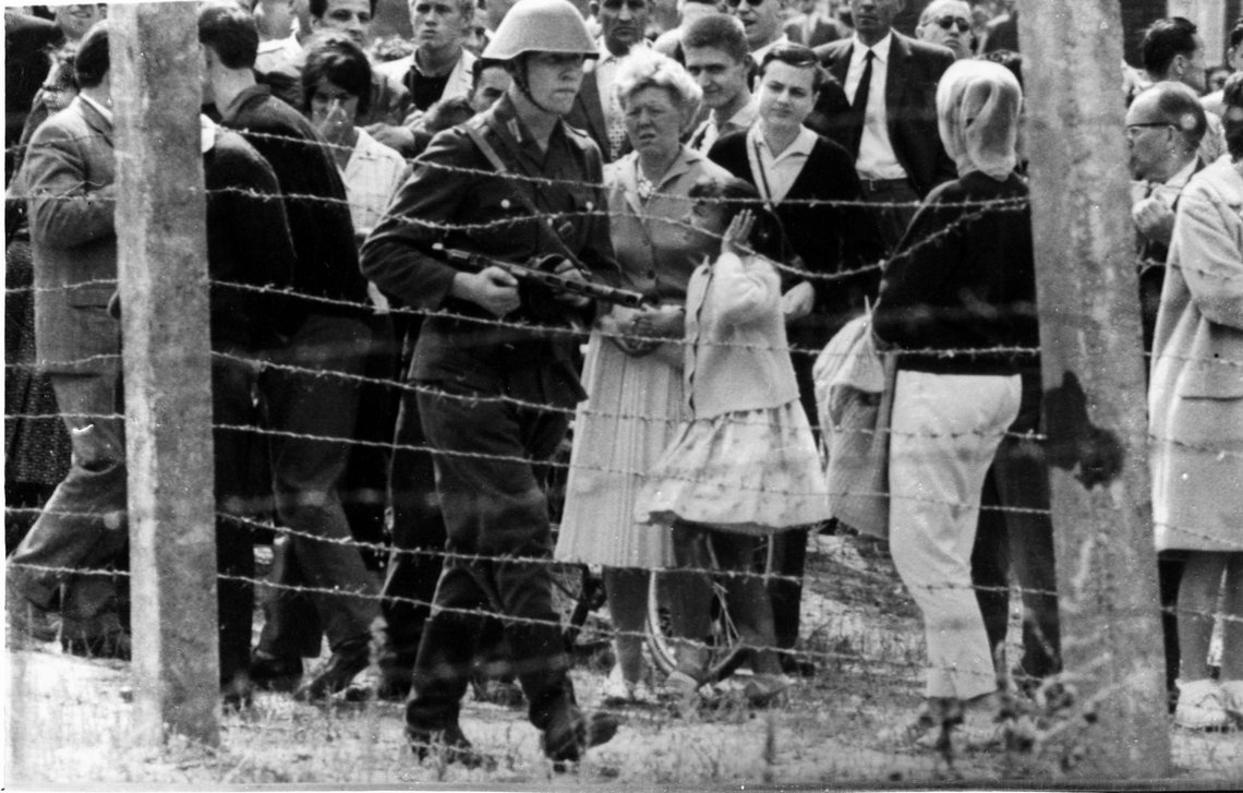 13. august 1961: Byggingen av Berlin-muren som skal skille Øst- og Vest-Berlin er i gang. Enkelte steder er det foreløpig bare en godt bevoktet piggtråd som deler Berlin. Her patruljerer en østtysk soldat med våpen langs et piggtrådgjerde på vesttysk side. Foto: UPI / NTB / arkiv 13. august 1961: Byggingen av Berlin-muren som skal skille Øst- og Vest-Berlin er i gang. Enkelte steder er det foreløpig bare en godt bevoktet piggtråd som deler Berlin. Her patruljerer en østtysk soldat med våpen langs et piggtrådgjerde på vesttysk side. Foto: UPI / NTB / arkiv