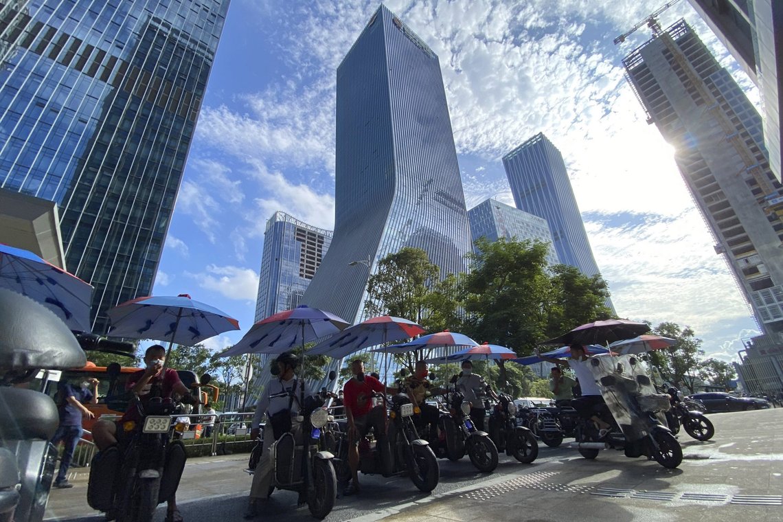 FILE - In this Sept. 24, file photo, men on electric bikes wait for riders near the Evergrande headquarters, center, in Shenzhen, China. Shares in troubled real estate developer China Evergrande Group and its property management unit Evergrande Property Services have been suspended from trading in Hong Kong, Monday, Oct. 4, 2021. (AP Photo/Ng Han Guan, File) FILE - In this Sept. 24, file photo, men on electric bikes wait for riders near the Evergrande headquarters, center, in Shenzhen, China. Shares in troubled real estate developer China Evergrande Group and its property management unit Evergrande Property Services have been suspended from trading in Hong Kong, Monday, Oct. 4, 2021. (AP Photo/Ng Han Guan, File)
