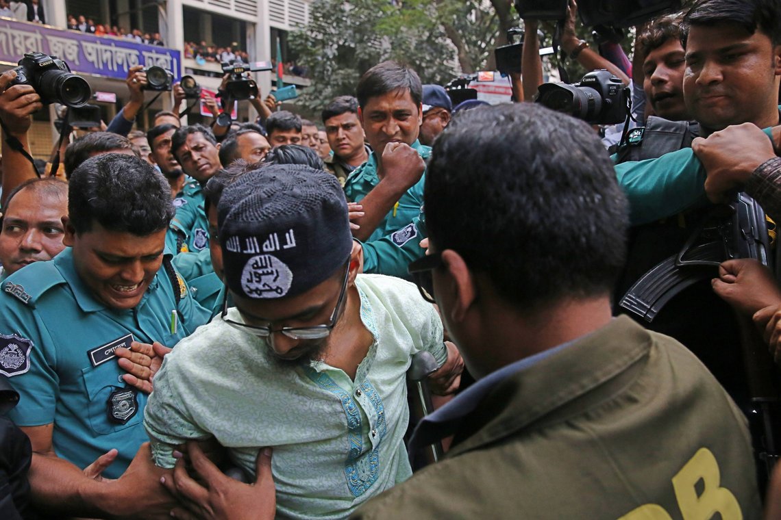 På dette arkivbildet fra 2019 eskorterer politiet et medlem av den forbudte islamistgruppen Jumatul Mujahedeen Bangladesh Group, etter at han ble dømt til døden for et angrep på en Dhaka-kafé som drepte mer enn 20 personer i Dhaka, Bangladesh, onsdag 27. november 2019. Den samme gruppen sto bak et angrep på en kafé 1.7.16. Fem islamister tok da flere kafegjester som gisler. Tjue gisler ble drept, inkludert 17 fra Japan, Italia og India. Nå ønsker regjeringspartiet å endre landets grunnlov til igjen å bli sekulær. Foto: Mahmud Hossain Opu / AP / NTB På dette arkivbildet fra 2019 eskorterer politiet et medlem av den forbudte islamistgruppen Jumatul Mujahedeen Bangladesh Group, etter at han ble dømt til døden for et angrep på en Dhaka-kafé som drepte mer enn 20 personer i Dhaka, Bangladesh, onsdag 27. november 2019. Den samme gruppen sto bak et angrep på en kafé 1.7.16. Fem islamister tok da flere kafegjester som gisler. Tjue gisler ble drept, inkludert 17 fra Japan, Italia og India. Nå ønsker regjeringspartiet å endre landets grunnlov til igjen å bli sekulær. Foto: Mahmud Hossain Opu / AP / NTB