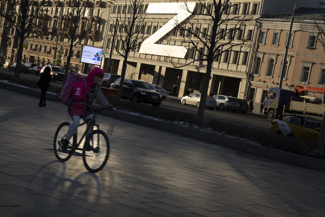 A food delivery courier rides a bicycle along a street with a huge letter Z, which has become a symbol of the Russian military, and a hashtag reading "We don't abandon our own" on a building during sunset in Moscow, Russia, Wednesday, March 30, 2022. (AP Photo) A food delivery courier rides a bicycle along a street with a huge letter Z, which has become a symbol of the Russian military, and a hashtag reading "We don't abandon our own" on a building during sunset in Moscow, Russia, Wednesday, March 30, 2022. (AP Photo)