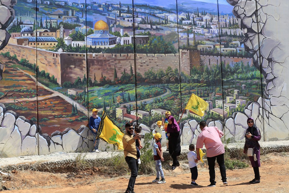 Hezbollah supporters wave Hezbollah flags in front of a poster shows the Dome of the Rock Mosque in the Al Aqsa Mosque painted on a wall that build by Israel, at the Lebanese-Israeli border, as they mark "Liberation Day" the twenty second anniversary of Israel's withdrawal from southern Lebanon in May 25, 2000, in Kfar Kila village, Southern Lebanon, Wednesday, May 25, 2022. (AP Photo/Mohammed Zaatari) Hezbollah supporters wave Hezbollah flags in front of a poster shows the Dome of the Rock Mosque in the Al Aqsa Mosque painted on a wall that build by Israel, at the Lebanese-Israeli border, as they mark "Liberation Day" the twenty second anniversary of Israel's withdrawal from southern Lebanon in May 25, 2000, in Kfar Kila village, Southern Lebanon, Wednesday, May 25, 2022. (AP Photo/Mohammed Zaatari)