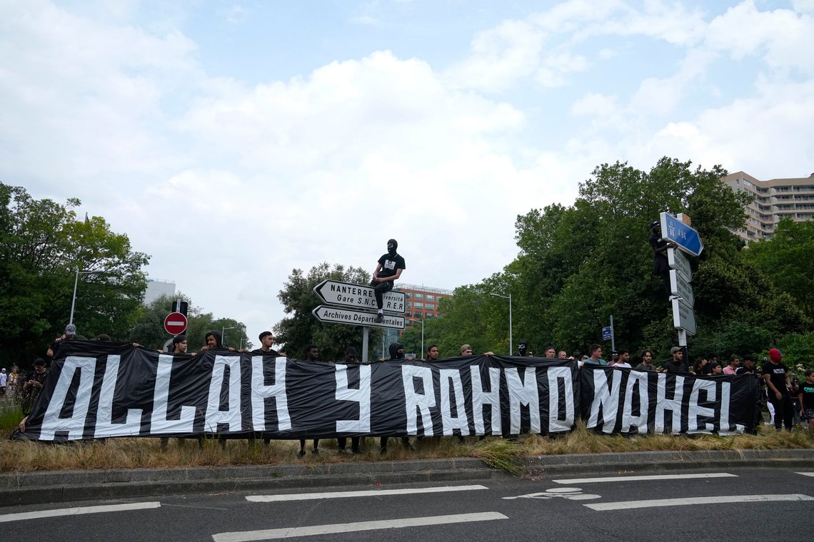 A man sits on a road sign above a banner reading "Allah, mercy for Nahel" during a march for Nahel, Thursday, June 29, 2023 in Nanterre, outside Paris. The killing of Nahel during a traffic check Tuesday, captured on video, shocked the country and stirred up long-simmering tensions between young people and police in housing projects and other disadvantaged neighborhoods around France. A French police officer who shot and killed a 17-year-old driver will be investigated for voluntary homicide, following two days of fires and violent protests officials said. (AP Photo/Michel Euler) A man sits on a road sign above a banner reading "Allah, mercy for Nahel" during a march for Nahel, Thursday, June 29, 2023 in Nanterre, outside Paris. The killing of Nahel during a traffic check Tuesday, captured on video, shocked the country and stirred up long-simmering tensions between young people and police in housing projects and other disadvantaged neighborhoods around France. A French police officer who shot and killed a 17-year-old driver will be investigated for voluntary homicide, following two days of fires and violent protests officials said. (AP Photo/Michel Euler)