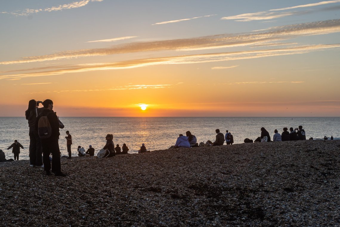 Brighton, UK - November 13th 2022: Golden clouds and sky as the sun sets on the horizon in front of people watching on Brighton Beach. Photo: Shutterstock by Pablo L Mendoza, United Kingdom. Brighton, UK - November 13th 2022: Golden clouds and sky as the sun sets on the horizon in front of people watching on Brighton Beach. Photo: Shutterstock by Pablo L Mendoza, United Kingdom.