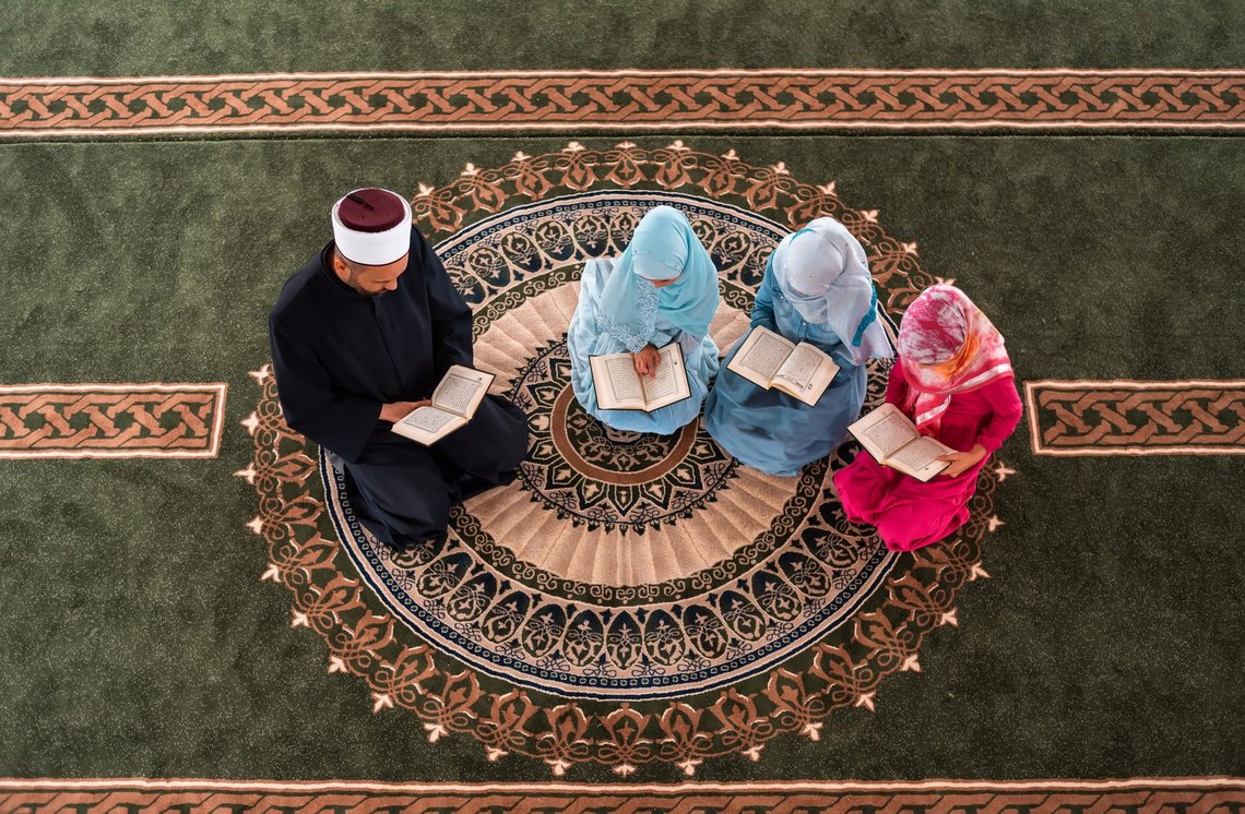 A Muslim teacher teaches children girls to read a holy book Quran inside the Mosque group of Islamic people praying inside the masjid. Photo: Shutterstock by MalikNalik. A Muslim teacher teaches children girls to read a holy book Quran inside the Mosque group of Islamic people praying inside the masjid. Photo: Shutterstock by MalikNalik.