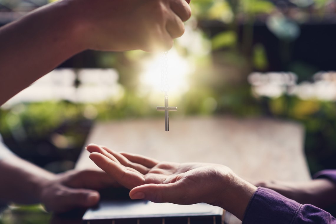 Christian hands giving cross necklace to friend. Christian prayer. Photo: Shutterstock by palidachan, Thailand. Christian hands giving cross necklace to friend. Christian prayer. Photo: Shutterstock by palidachan, Thailand.