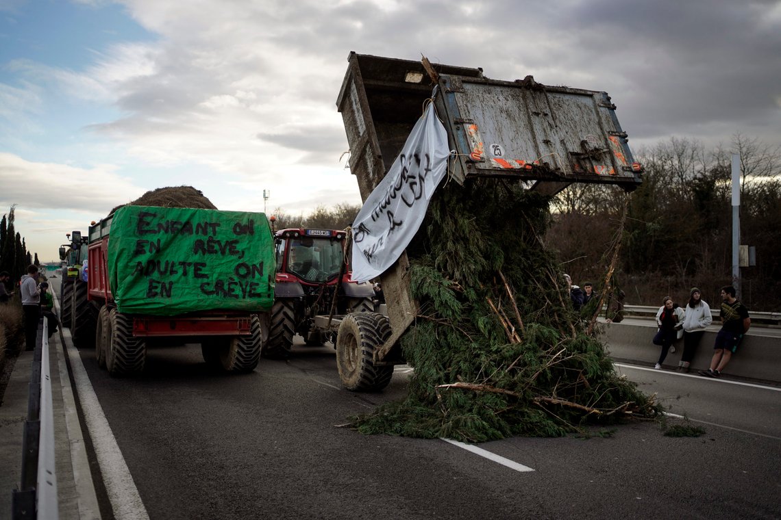 Farmers unload trees as they invade the motorway near Lyon, central France, Wednesday, Jan. 24, 2024. French farmers protest across the country and in Brussels against low wages and what they consider to be excessive regulation, mounting costs and other problems. Banner at right reads: the world is upside down. Banner at left reads: farming, a childhood dream that kills us as adults. (AP Photo/Laurent Cipriani) Farmers unload trees as they invade the motorway near Lyon, central France, Wednesday, Jan. 24, 2024. French farmers protest across the country and in Brussels against low wages and what they consider to be excessive regulation, mounting costs and other problems. Banner at right reads: the world is upside down. Banner at left reads: farming, a childhood dream that kills us as adults. (AP Photo/Laurent Cipriani)
