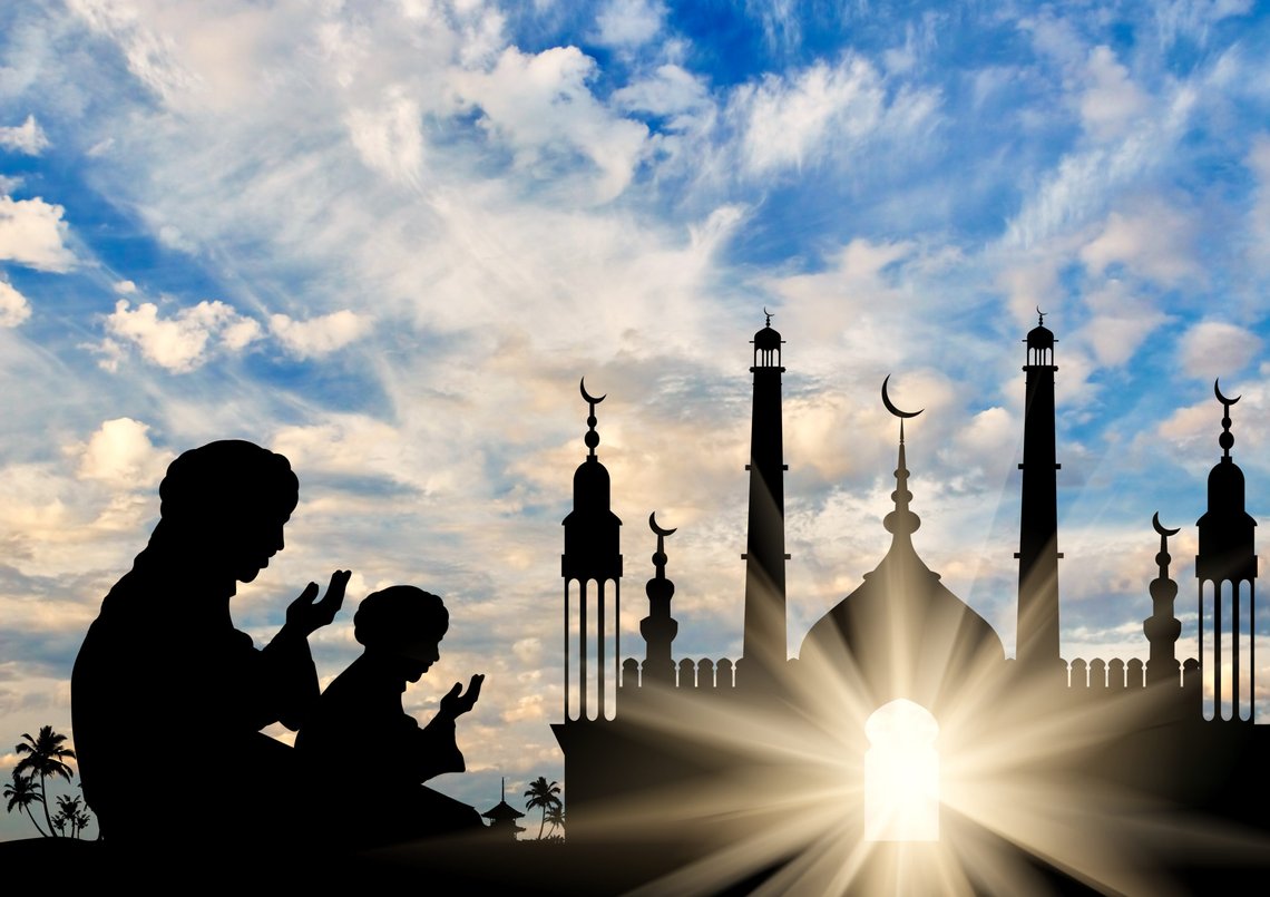 Concept of the Islamic religion. Silhouette of two men praying on the background of the town hall at dawn. Photo: Shutterstock by Prazis Images, Ukraine. Concept of the Islamic religion. Silhouette of two men praying on the background of the town hall at dawn. Photo: Shutterstock by Prazis Images, Ukraine.