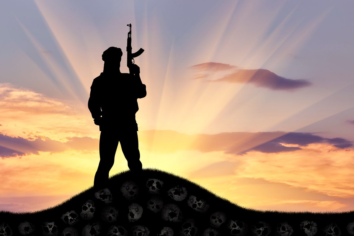 Concept of terrorism. Silhouette of a terrorist with a rifle standing on a pile of skulls at sunset. Photo: Shutterstock by Prazis Images, Ukraina. Concept of terrorism. Silhouette of a terrorist with a rifle standing on a pile of skulls at sunset. Photo: Shutterstock by Prazis Images, Ukraina.