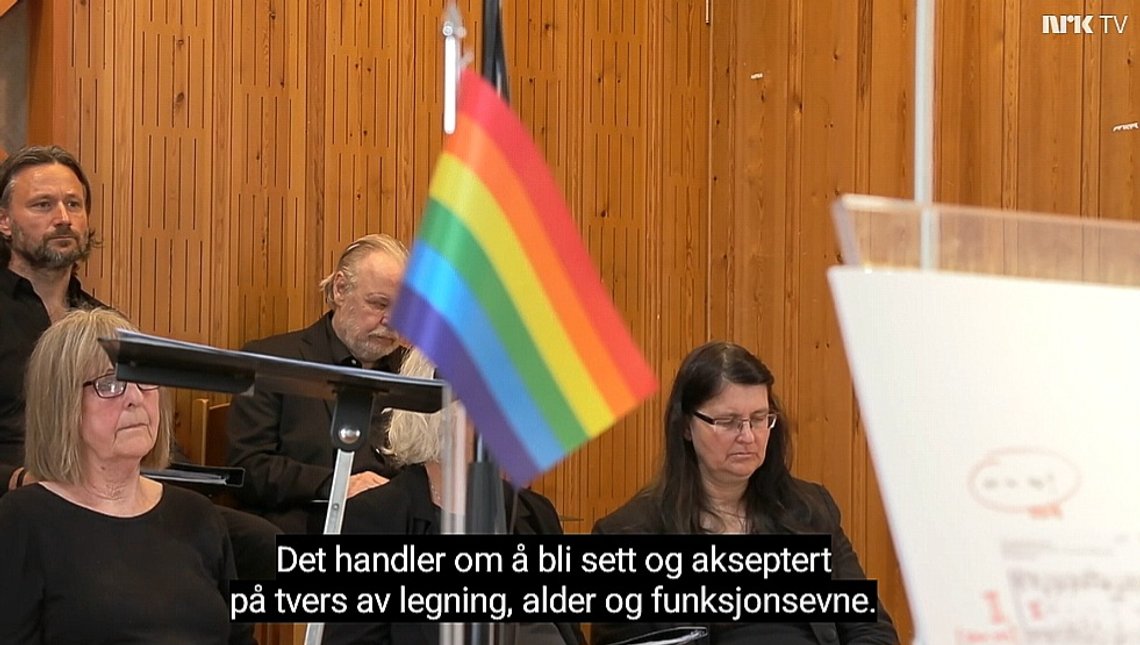 Pride-flagget var ikke stort, men tydelig til stede gjennom hele søndagsgudstjnesten fra Bodø domkirke, vist i NRK 9. juni 2024. I bakgrunnen medlemmer av kirkekoret. Skjermdump. Pride-flagget var ikke stort, men tydelig til stede gjennom hele søndagsgudstjnesten fra Bodø domkirke, vist i NRK 9. juni 2024. I bakgrunnen medlemmer av kirkekoret. Skjermdump.