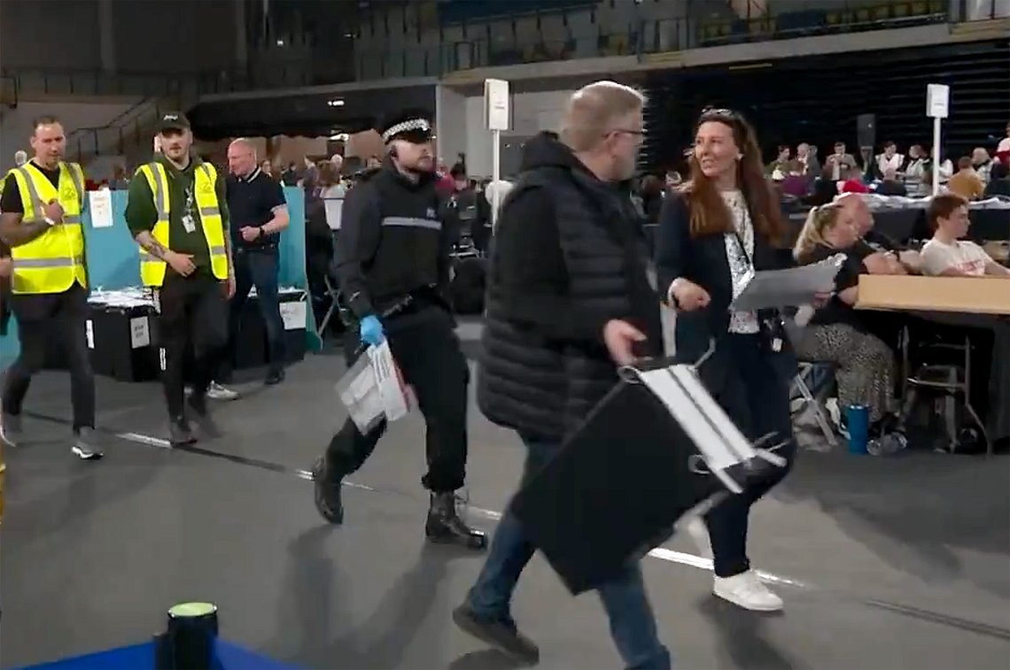 Skotsk politi bærer ut stemmesedler fra Emirates Stadium i Glasgow sent torsdag kveld. (Foto: Stillbilde fra video/STV News på X) Politifolk i Skottland bærer ut bevismateriale