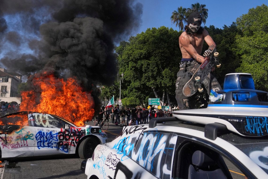A protester vandalizes a Waymo taxi as another burns near the metropolitan detention center of downtown Los Angeles, Sunday, June 8, 2025, following last night's immigration raid protest. (AP Photo/Jae C. Hong) A protester vandalizes a Waymo taxi as another burns near the metropolitan detention center of downtown Los Angeles, Sunday, June 8, 2025, following last night's immigration raid protest. (AP Photo/Jae C. Hong)