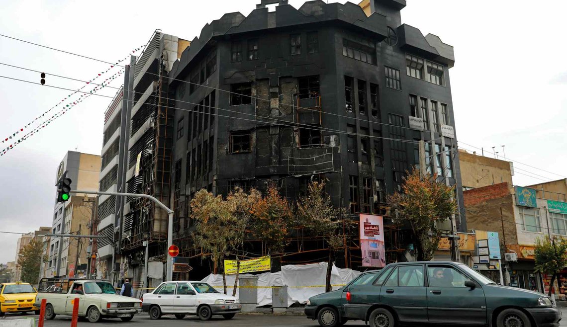 Biler i Teheran passerer en bygning som ble satt i brann under protestene mot regjeringens økning i bensinprisene i november 2019. Demonstrasjonene bredte seg til minst 100 byer og tettsteder og eskalerte til voldelige sammenstøt der banker, butikker og politistasjoner ble angrepet og brent ned. (Foto: AP Photo/Ebrahim Noroozi.) Biler i Teheran passerer en bygning som ble satt i brann under protestene mot regjeringens økning i bensinprisene i november 2019. Demonstrasjonene bredte seg til minst 100 byer og tettsteder og eskalerte til voldelige sammenstøt der banker, butikker og politistasjoner ble angrepet og brent ned. (Foto: AP Photo/Ebrahim Noroozi.)