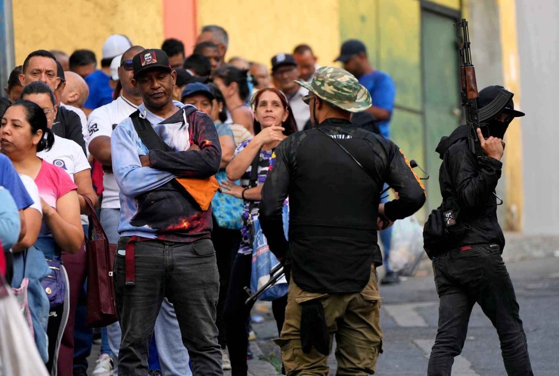 Væpnede vakter fra en regimelojal gjeng av "colectivos" vokter køen for å komme inn på et supermarked i Caracas, Venezuela, dagen etter at Nicolás Maduro ble pågrepet og fraktet til USA. (Foto: Ariana Cubillos/AP Photo) Væpnede vakter fra en regimelojal gjeng av "colectivos" vokter køen for å komme inn på et supermarked i Caracas, Venezuela, dagen etter at Nicolás Maduro ble pågrepet og fraktet til USA. (Foto: Ariana Cubillos/AP Photo)