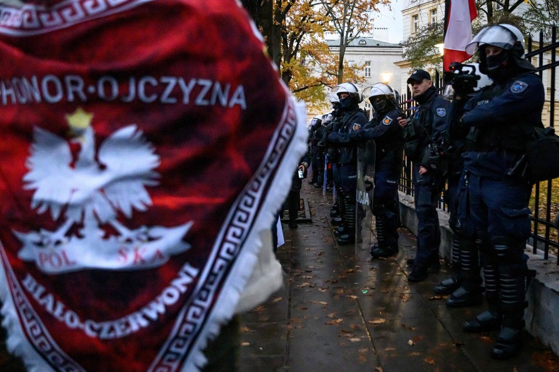TOPSHOT - A protester wearing a Polish insignia shawl walks in front of the riot police positioned outside the headquarters of Poland's Constitutional Court in Warsaw during a protest on October 31, 2026. Poland's President Karol Nawrocki called off a visit to Africa in mid-flight as riot police deployed around the country's constitutional court on October 30 following the suspension of its chief justice in a battle between the centrist government and the nationalist right. Dozens of police guarded the entrance to the court as followers of the opposition right-wing Law and Justice party (PiS) protested the ousting of constitutional court president Bogdan Swieczkowski. (Photo by Mladen ANTONOV / AFP) TOPSHOT - A protester wearing a Polish insignia shawl walks in front of the riot police positioned outside the headquarters of Poland's Constitutional Court in Warsaw during a protest on October 31, 2026. Poland's President Karol Nawrocki called off a visit to Africa in mid-flight as riot police deployed around the country's constitutional court on October 30 following the suspension of its chief justice in a battle between the centrist government and the nationalist right. Dozens of police guarded the entrance to the court as followers of the opposition right-wing Law and Justice party (PiS) protested the ousting of constitutional court president Bogdan Swieczkowski. (Photo by Mladen ANTONOV / AFP)
