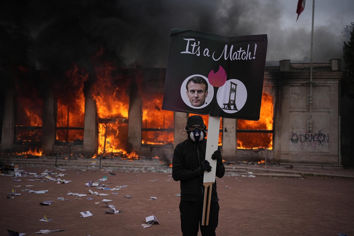 A protester holds a board with a photo of French president Emmanuel Macron in front of a burning tourism office during a demonstration against rising living costs and in solidarity with students’ grievances in Lyon, France, Saturday, Oct. 17, 2026. (AP Photo/Laurent Cipriani) A protester holds a board with a photo of French president Emmanuel Macron in front of a burning tourism office during a demonstration against rising living costs and in solidarity with students’ grievances in Lyon, France, Saturday, Oct. 17, 2026. (AP Photo/Laurent Cipriani)