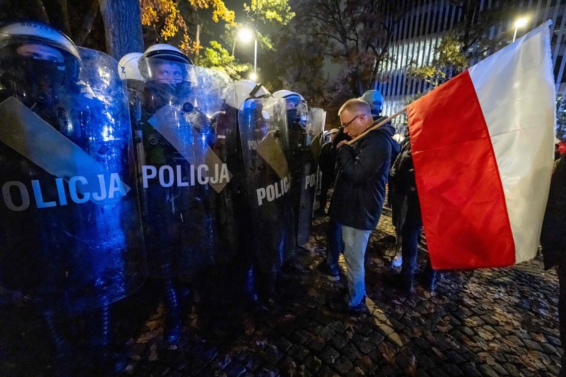 En mann med det polske flagget står foran opprørspoliti mens demonstranter samler seg utenfor Polens grunnlovsdomstol i Warszawa, etter at politiet sperret adgangen til bygningen 30. oktober 2026.
Flere titalls politifolk bevoktet inngangen til domstolen mens tilhengere av opposisjonspartiet Lov og rettferdighet (PiS) protesterte mot avsettelsen av domstolens president Bogdan Święczkowski. (Foto: Wojtek Radwanski / AFP) En mann med det polske flagget står foran opprørspoliti mens demonstranter samler seg utenfor Polens grunnlovsdomstol i Warszawa, etter at politiet sperret adgangen til bygningen 30. oktober 2026.
Flere titalls politifolk bevoktet inngangen til domstolen mens tilhengere av opposisjonspartiet Lov og rettferdighet (PiS) protesterte mot avsettelsen av domstolens president Bogdan Święczkowski. (Foto: Wojtek Radwanski / AFP)