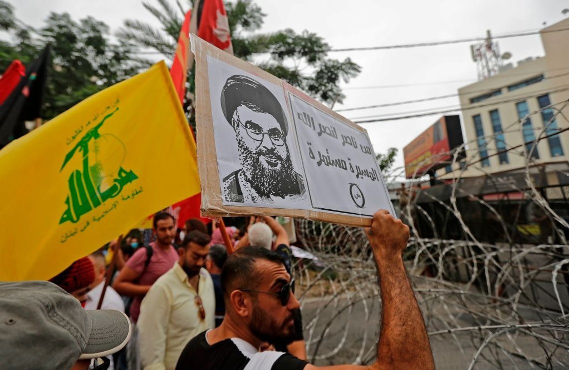 A protester stands with a flag of the Lebanese Shiite movement Hezbollah and holding up a sign showing the face of its leader Hassan Nasrallah, with text in Arabic reading "from Nasser to Nasrallah, the march continues" (referencing late Egyptian president Gamal Abdel Nasser), during an anti-US demonstration near the United States' Embassy headquarters in Awkar, northeast of Lebanon's capital Beirut on July 10, 2020. (Photo by JOSEPH EID / AFP) (Photo by JOSEPH EID/AFP via Getty Images) A protester stands with a flag of the Lebanese Shiite movement Hezbollah and holding up a sign showing the face of its leader Hassan Nasrallah, with text in Arabic reading "from Nasser to Nasrallah, the march continues" (referencing late Egyptian president Gamal Abdel Nasser), during an anti-US demonstration near the United States' Embassy headquarters in Awkar, northeast of Lebanon's capital Beirut on July 10, 2020. (Photo by JOSEPH EID / AFP) (Photo by JOSEPH EID/AFP via Getty Images)