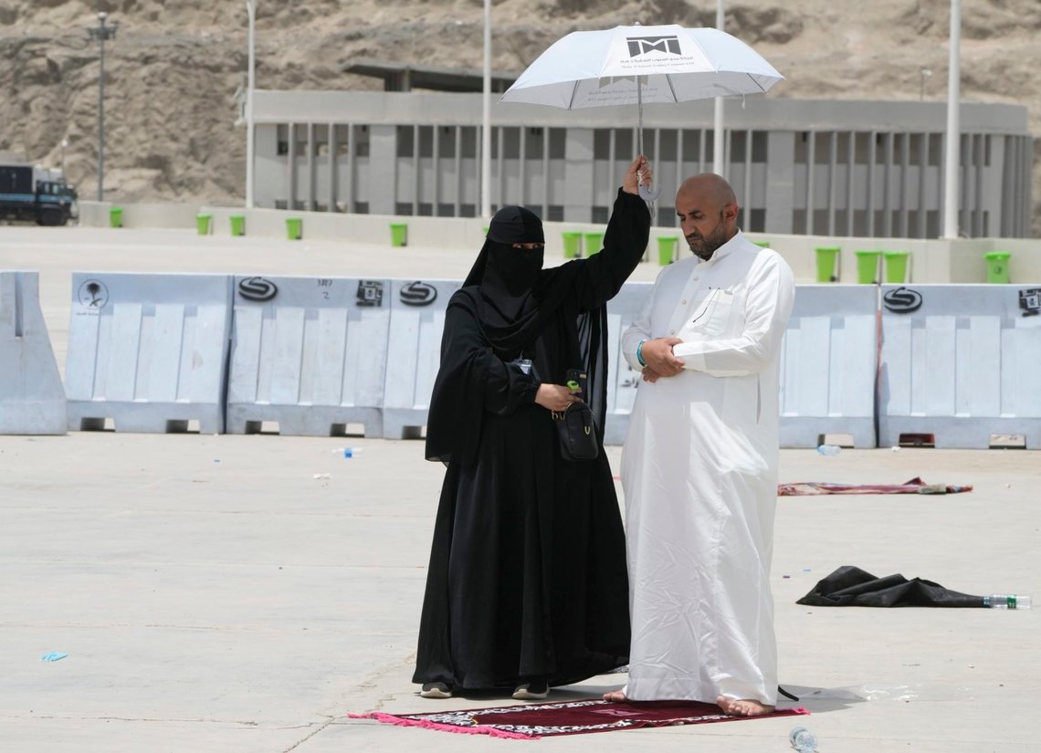 En beslöjad kvinna skyddar en man som ber under hajj i Mecka från solen den 11 juni 2022. Foto: Amr Nabil / AP / NTB. En beslöjad kvinna skyddar en man som ber under hajj i Mecka från solen den 11 juni 2022. Foto: Amr Nabil / AP / NTB.