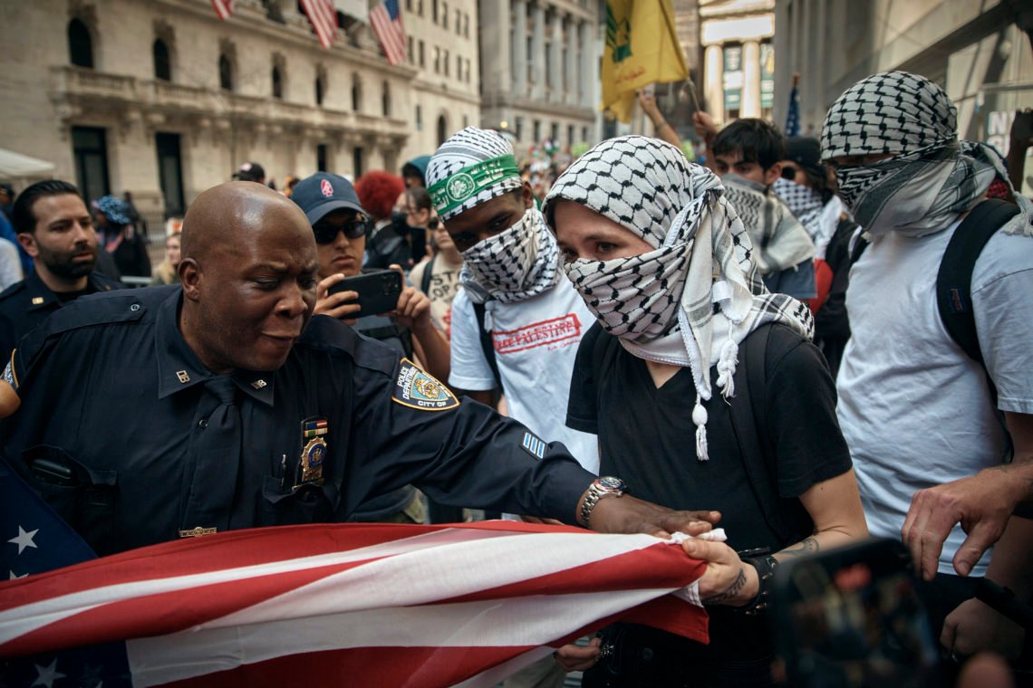 En pro-palestinsk demonstrant försöker ta tag i en amerikansk flagga från pro-israeliska anhängare under en demonstration utanför New York Stock Exchange, den 15 april 2024. Foto: Andres Kudacki / AP Photo En pro-palestinsk demonstrant försöker ta tag i en amerikansk flagga från pro-israeliska anhängare under en demonstration utanför New York Stock Exchange, den 15 april 2024. Foto: Andres Kudacki / AP Photo