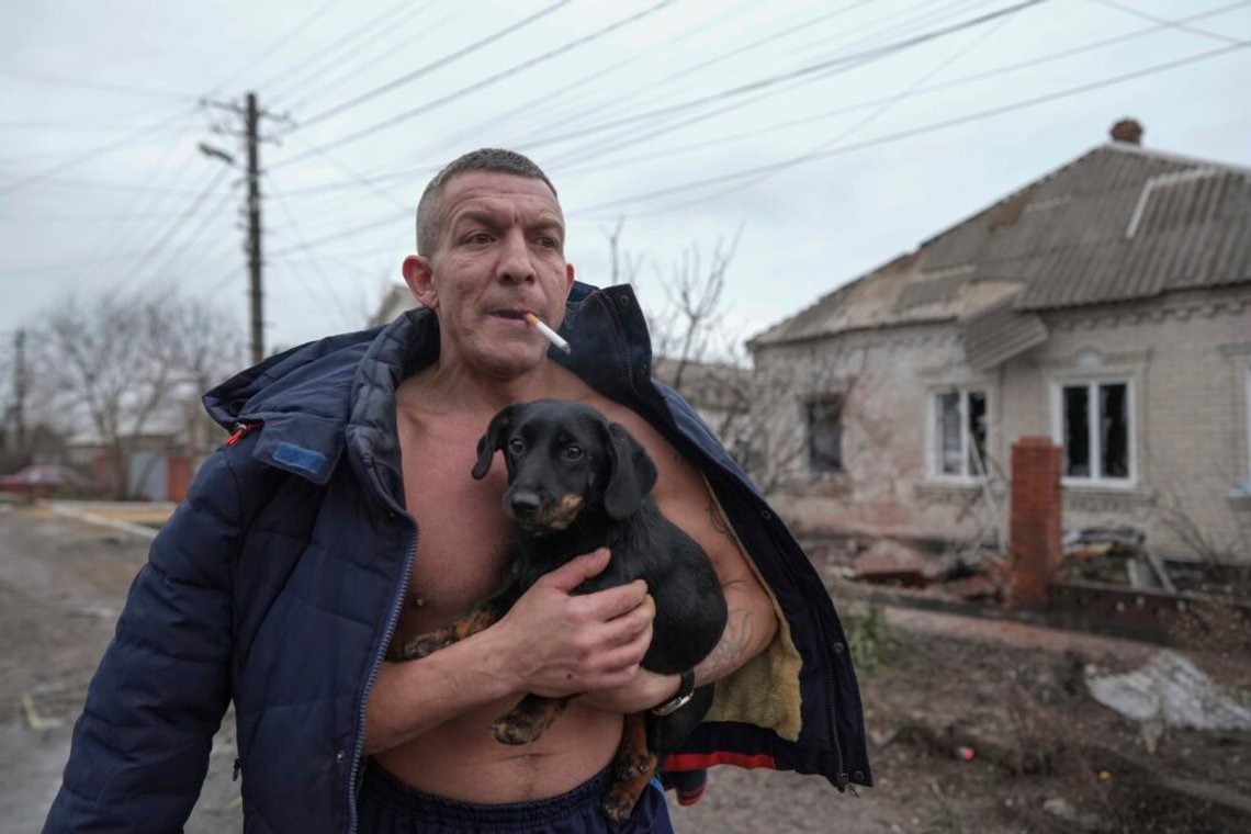 En man håller i en hund när han går förbi ett hus som skadats av rysk bombning i Mariupol, Ukraina, den 24 februari 2022. Foto: Evgeniy Maloletka / AP / NTB. En man håller i en hund när han går förbi ett hus som skadats av rysk bombning i Mariupol, Ukraina, den 24 februari 2022. Foto: Evgeniy Maloletka / AP / NTB.
