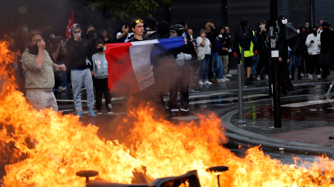 En aktivist från rörelsen Bloquons Tout ("Blockera allt") håller upp den franska flaggan nära brinnande soptunnor i Lille, norra Frankrike, den 10 september 2025. Foto: Jean-Francois Badias / AP / NTB. En aktivist från rörelsen Bloquons Tout ("Blockera allt") håller upp den franska flaggan nära brinnande soptunnor i Lille, norra Frankrike, den 10 september 2025. Foto: Jean-Francois Badias / AP / NTB.